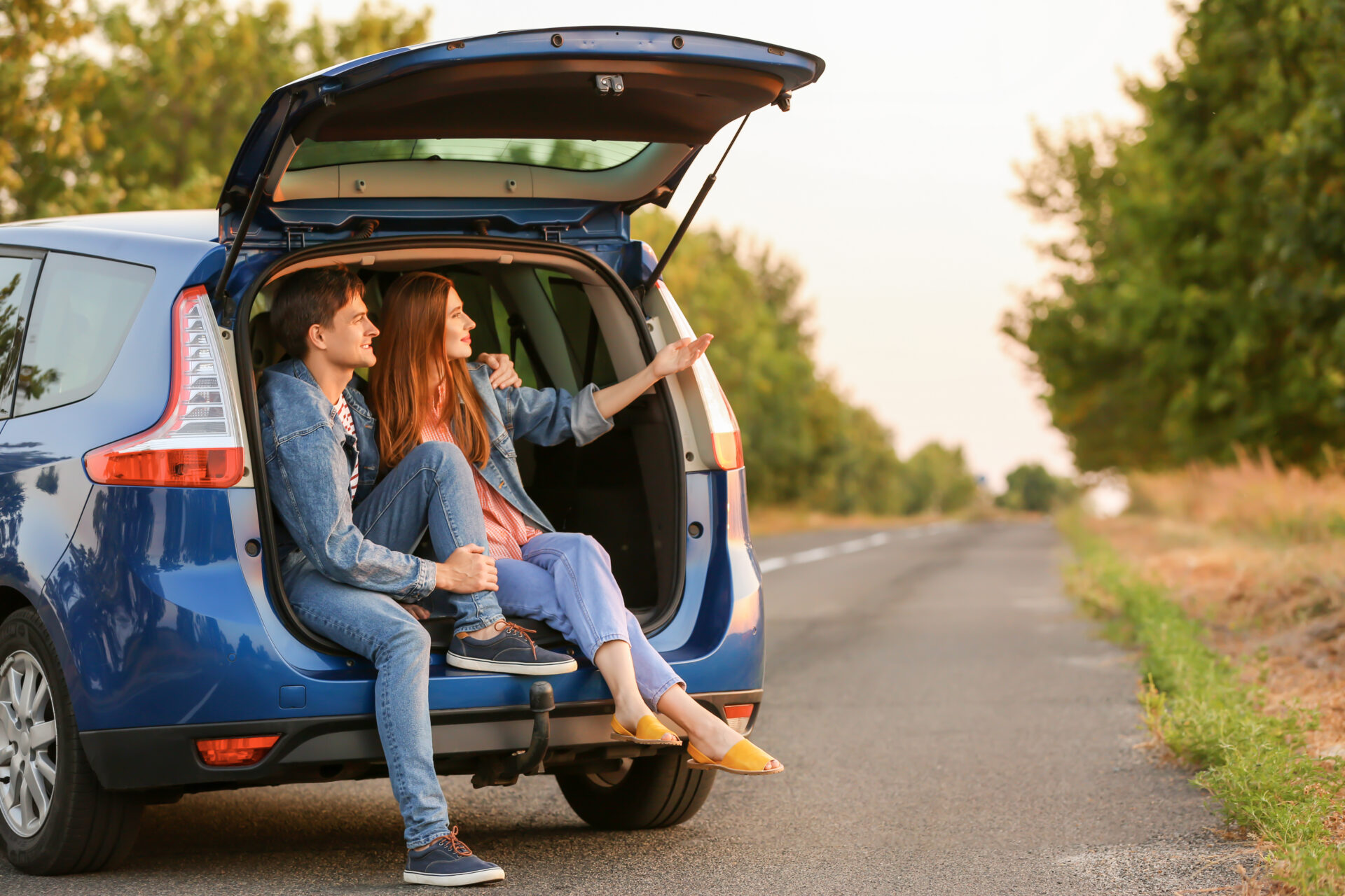 Happy couple sitting in trunk of their new car in countryside